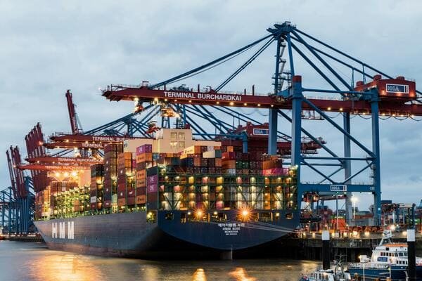 A cargo ship at a port with containers being unloaded, representing international trade.