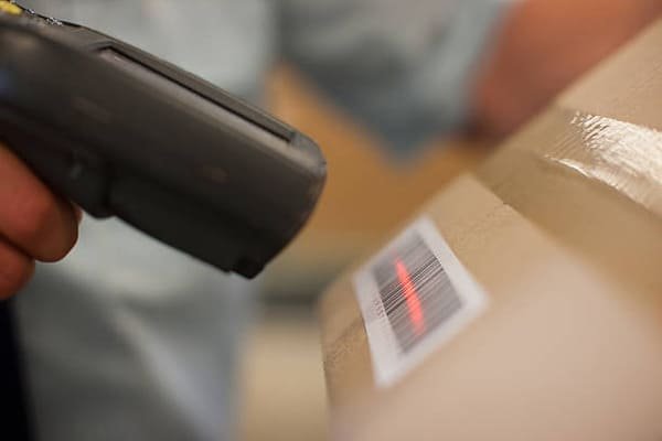 A customs official using a tablet to scan a barcode on a package, with data appearing on the screen.