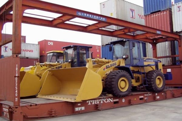A large yellow excavator being loaded onto a ship for overseas transport