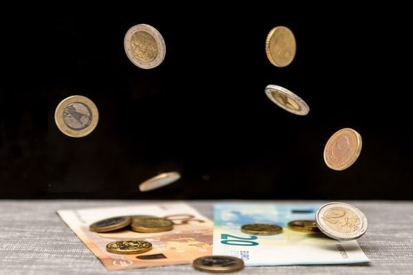 Euro coins and banknotes spill onto the table against a black background
